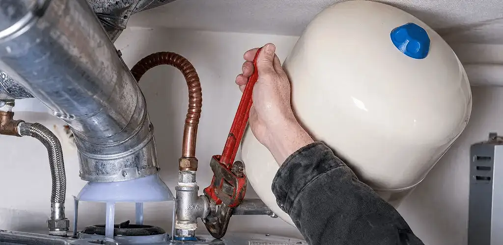 Water heater repair technician tightening plumbing connections near a tank unit in Stockton, CA